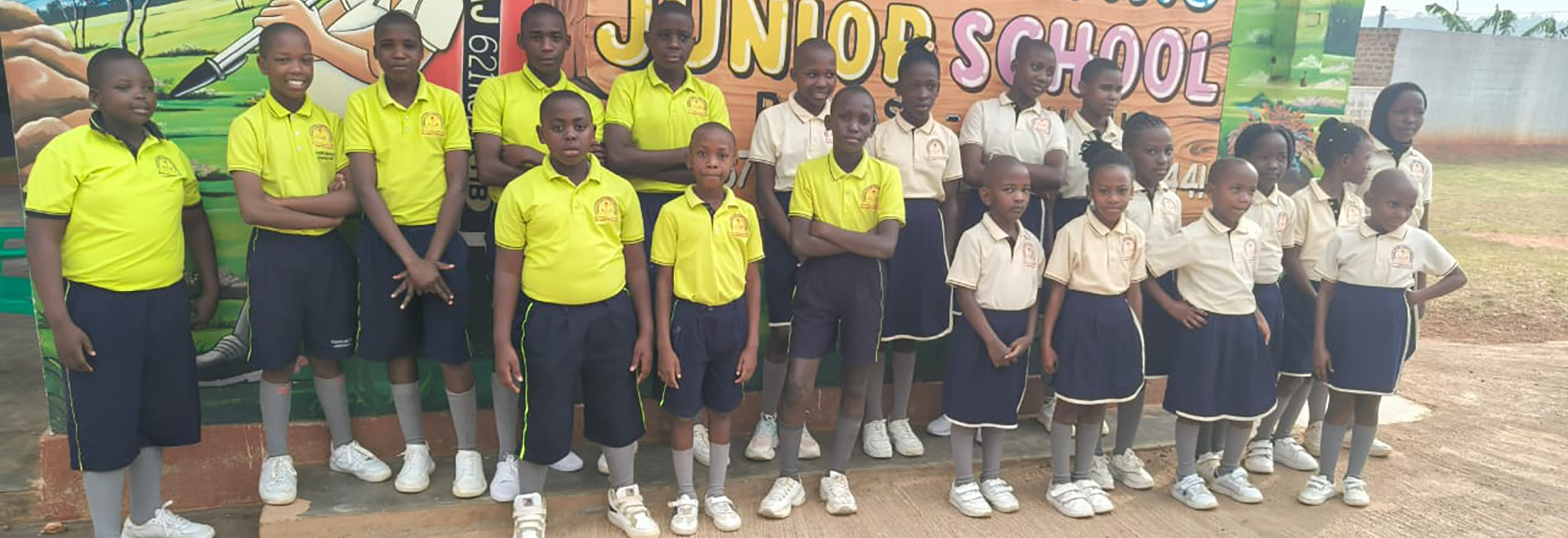 Proud BoldStars Junior School students posing confidently in front of a vibrant, illustrated school backdrop at the entrance.